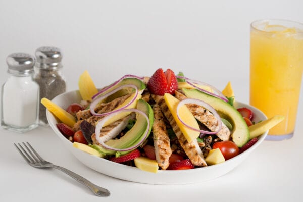A bowl of salad with chicken, mango and strawberries.