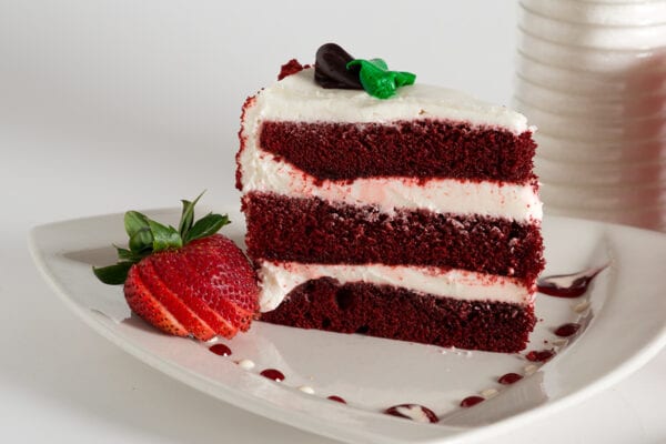 A slice of red velvet cake with white frosting and a strawberry on top.